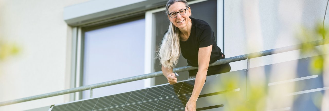 Frau steht auf einem Balkon, an dem ein Solarpanel angebracht ist