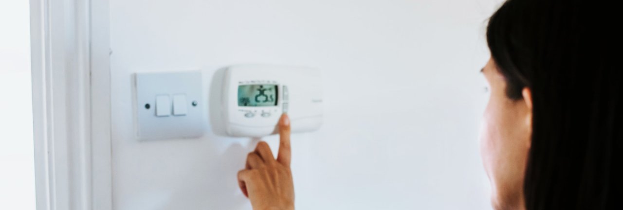 Person steht vor digitalem Thermostat und stellt die Raumtemperatur ein