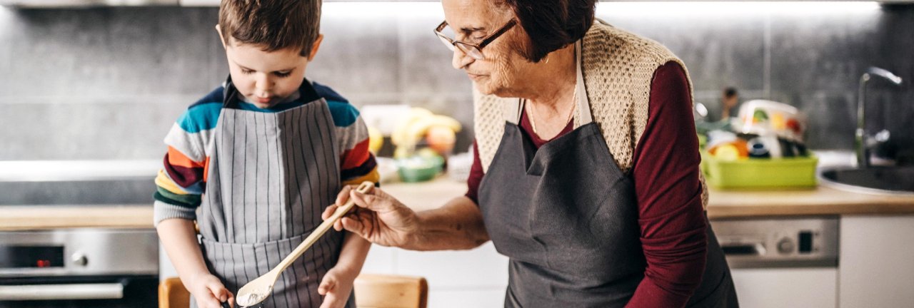 Ein Kind und eine ältere Frau stehen zusammen in der Küche und kochen