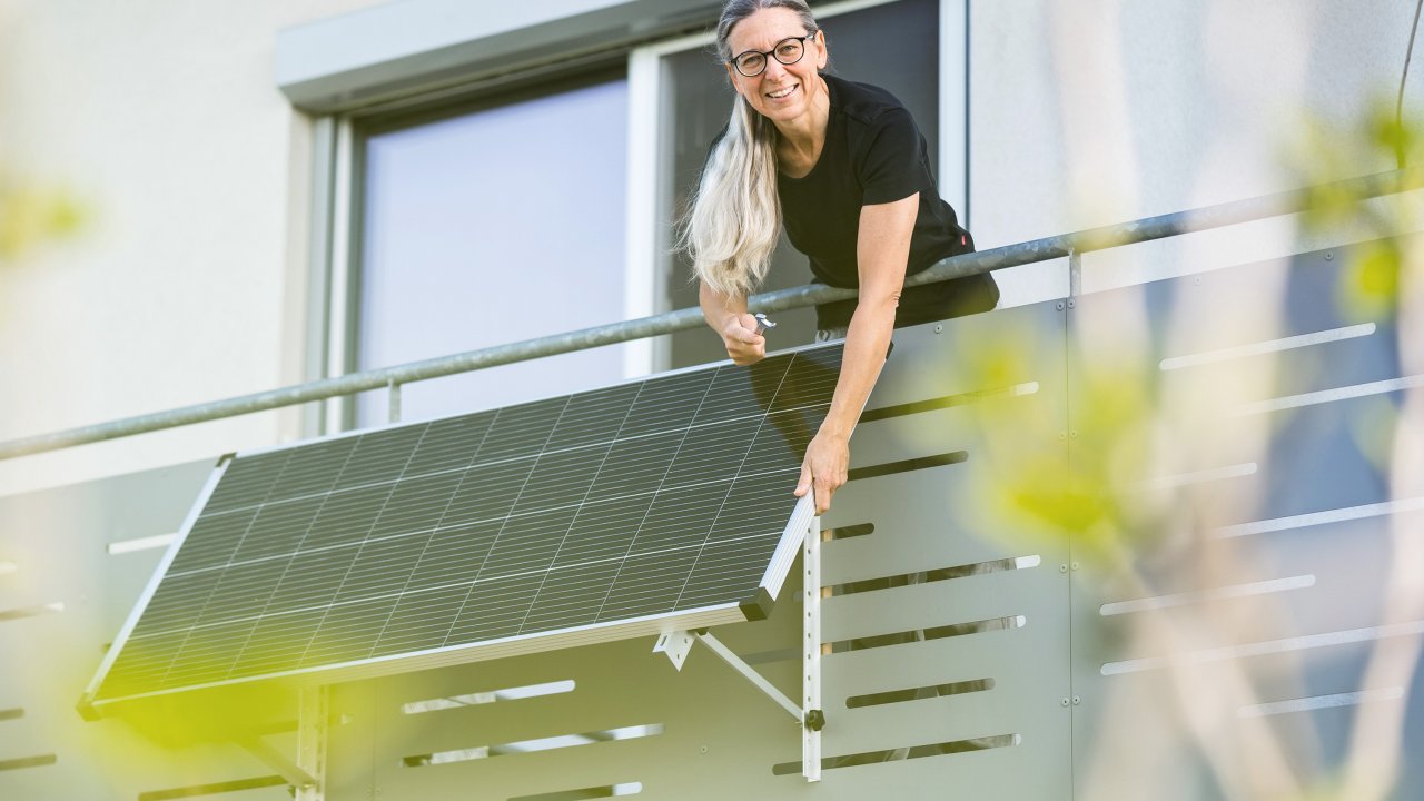 Frau steht auf einem Balkon, an dem ein Solarpanel angebracht ist