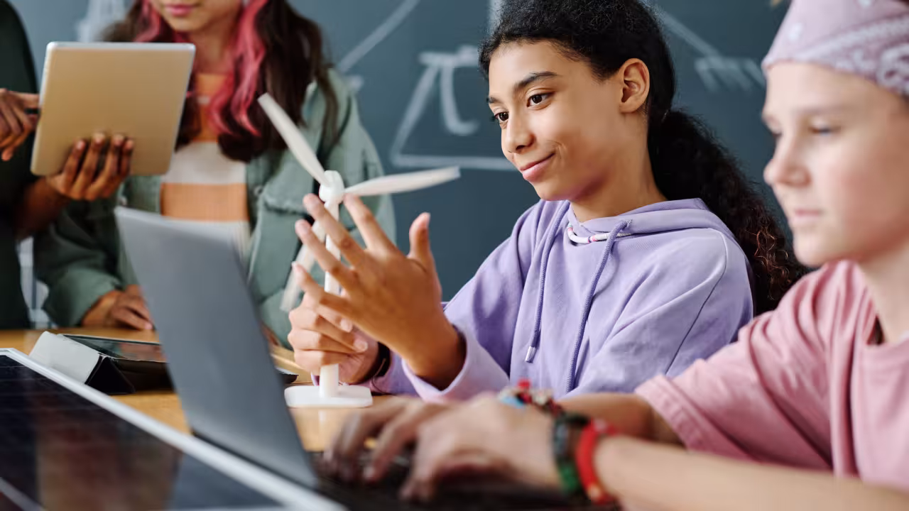 Schülerinnen sitzen am Tisch und betrachten das Modell eines Windrades