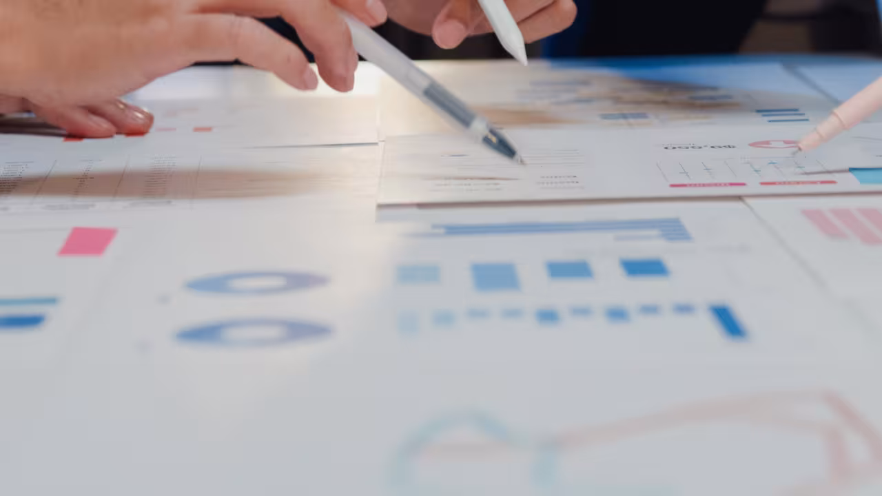 Hände von Menschen sind über ein Chart mit Zahlen und Grafiken gebeugt