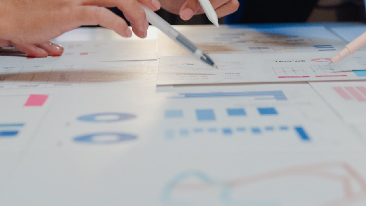 Hände von Menschen sind über ein Chart mit Zahlen und Grafiken gebeugt