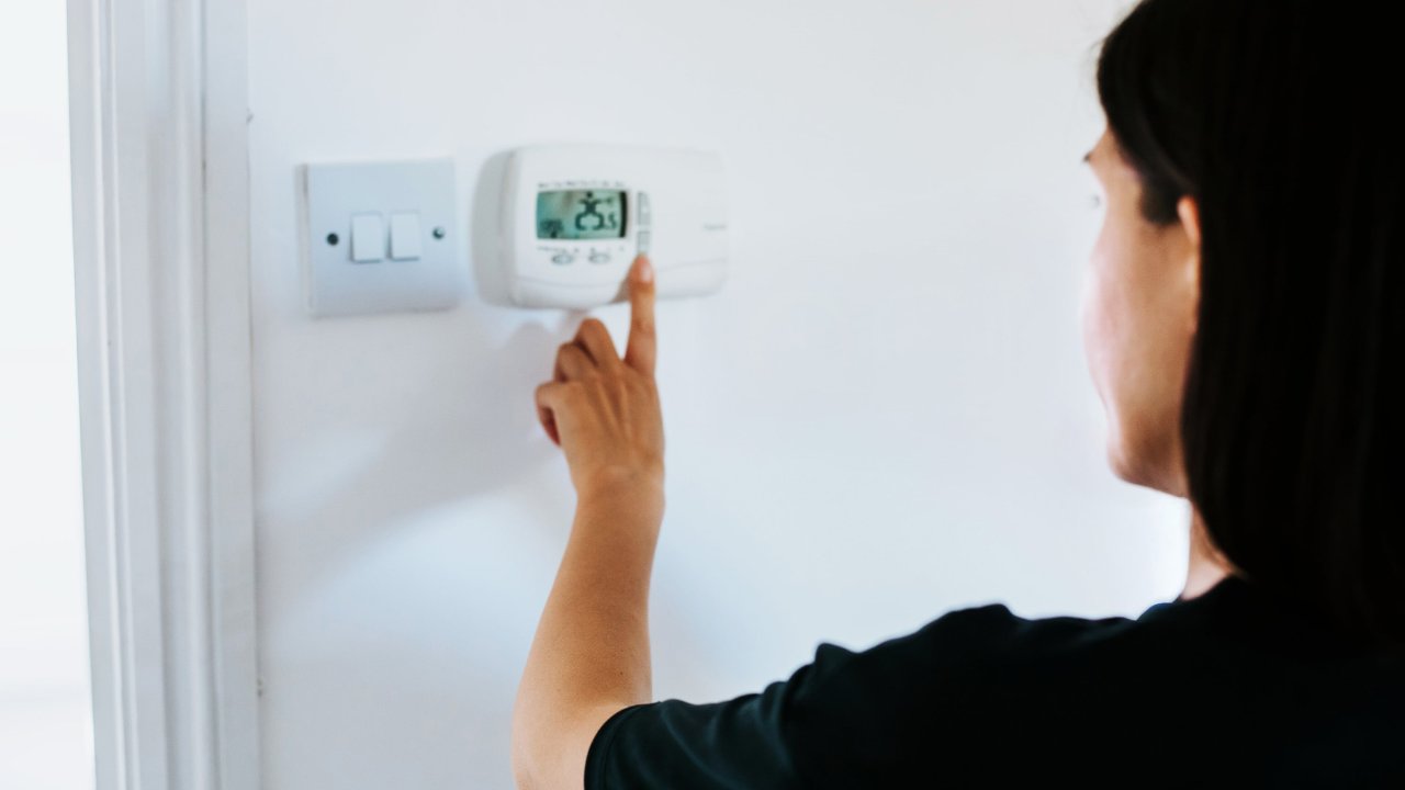Person steht vor digitalem Thermostat und stellt die Raumtemperatur ein
