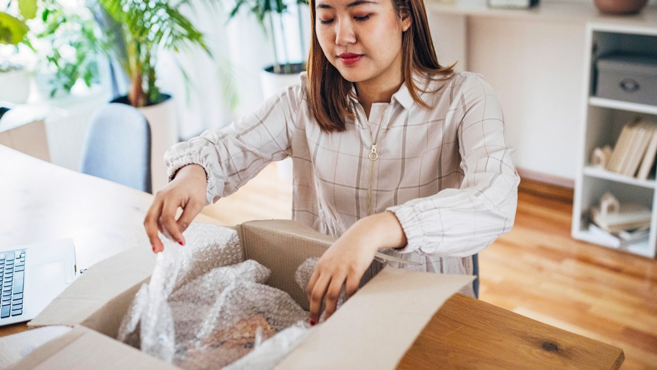 Eine Frau packt ein Paket aus, das vor ihr auf dem Tisch steht.