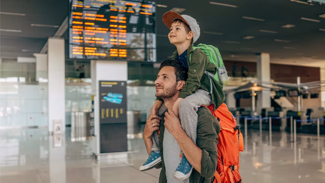 Ein Mann trägt ein Kind auf den Schultern durch ein Flughafen-Terminal.