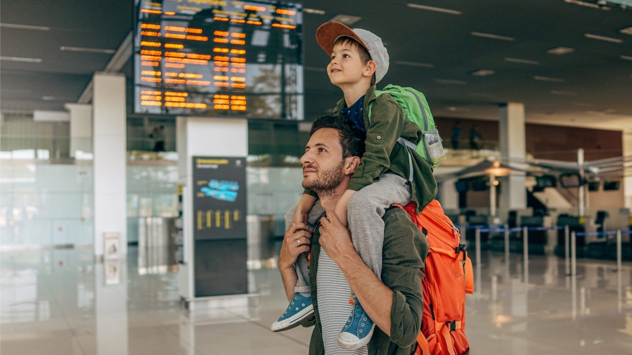 Ein Mann trägt ein Kind auf den Schultern durch ein Flughafen-Terminal.