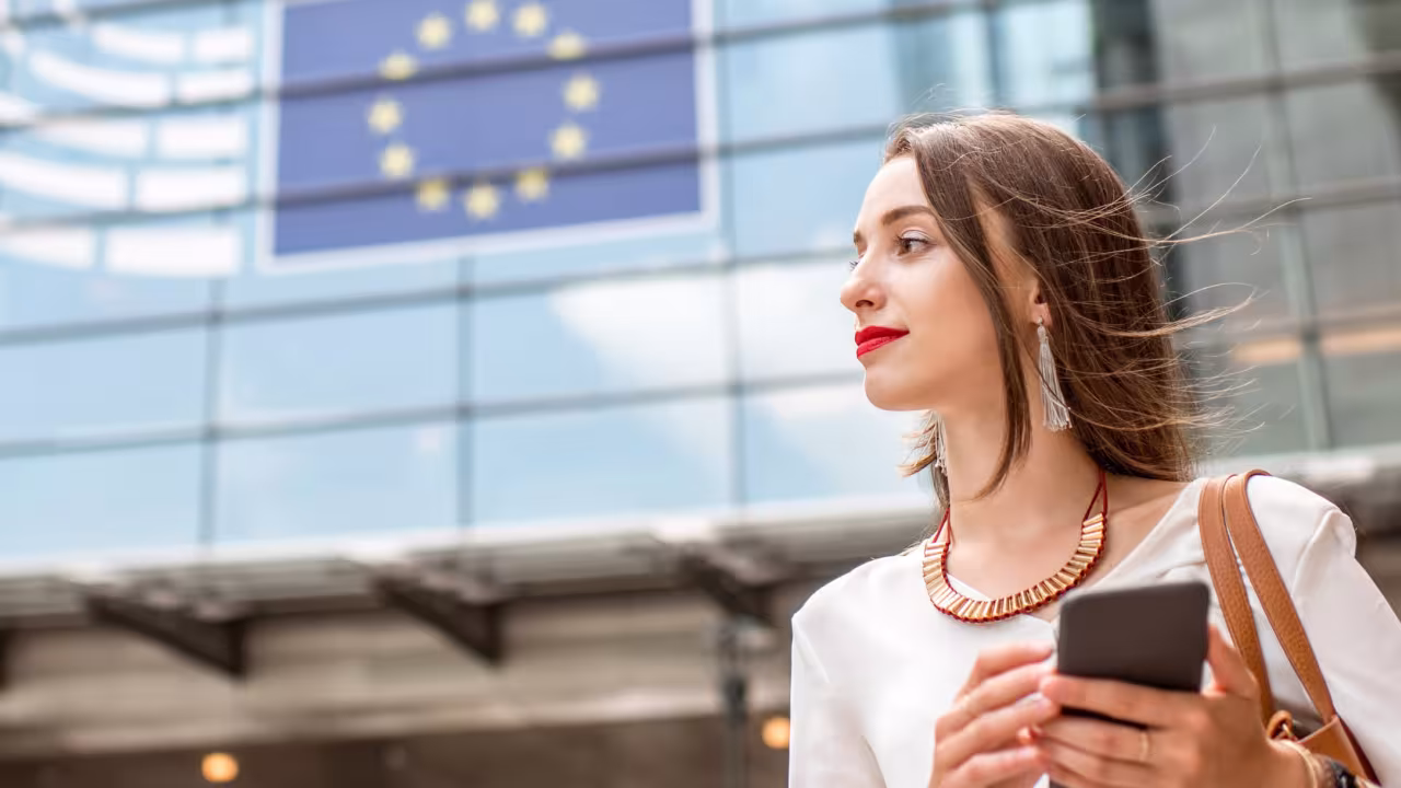 Eine Frau steht vor einem Regierungsgebäude der EU mit einem Handy in der Hand.